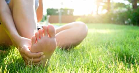 Barefoot woman sitting on the green grass thinking about athletes foot infection