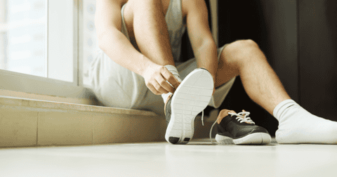Man putting his shoes on while sitting on the floor while thinking about athletes foot spread